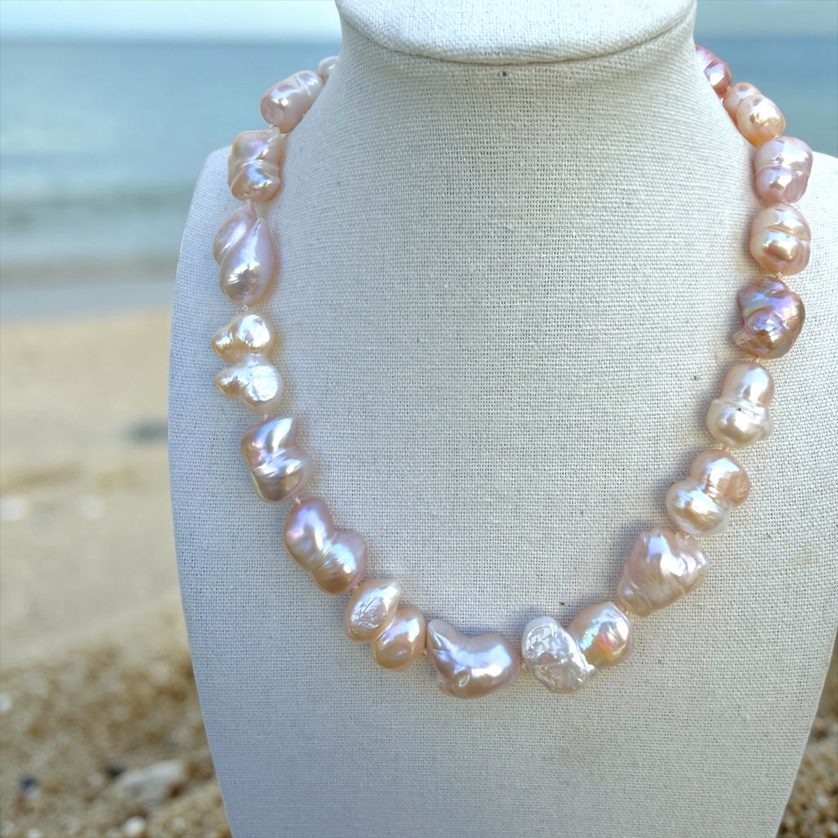 TNT Designs Jewels handcrafted blush pink baroque pearl statement necklace on a mannequin against a beach background.